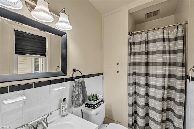 bathroom with tile walls, curtained shower, visible vents, toilet, and a sink