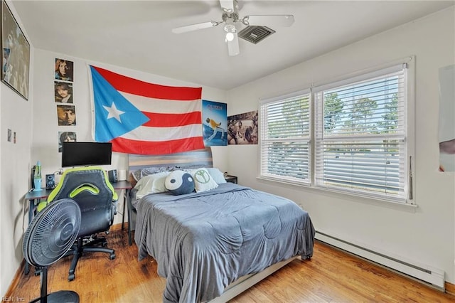 bedroom featuring a ceiling fan, visible vents, a baseboard heating unit, and wood finished floors