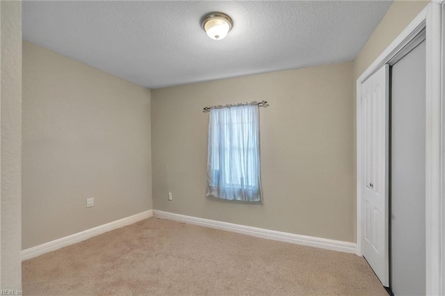 unfurnished bedroom featuring a textured ceiling, baseboards, a closet, and light colored carpet