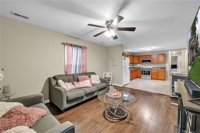 living room featuring baseboards, light wood-style flooring, visible vents, and a ceiling fan