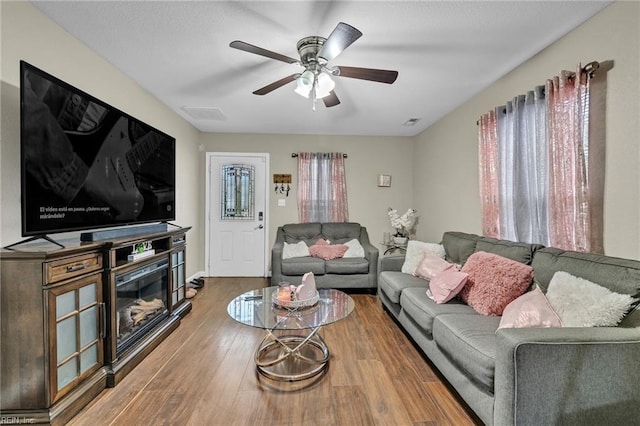 living room with ceiling fan, wood finished floors, and a glass covered fireplace