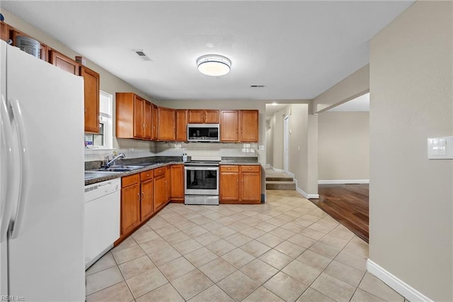 kitchen featuring light tile patterned floors, brown cabinetry, dark countertops, stainless steel appliances, and a sink