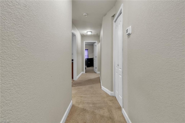 hall with baseboards, light colored carpet, and a textured wall