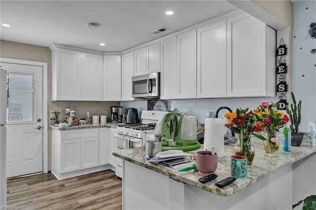 kitchen featuring light stone counters, visible vents, white cabinetry, stainless steel microwave, and white gas range