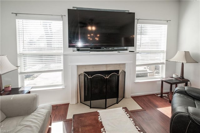 living room featuring a fireplace with flush hearth, baseboards, and wood finished floors