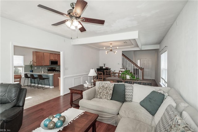 living area featuring ceiling fan with notable chandelier, wood finished floors, a raised ceiling, and stairs