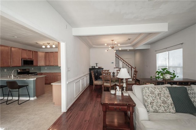 living area featuring a wainscoted wall, a raised ceiling, an inviting chandelier, ornamental molding, and stairs