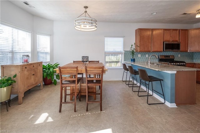 kitchen with visible vents, brown cabinetry, decorative backsplash, a breakfast bar area, and appliances with stainless steel finishes