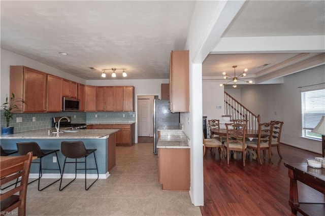 kitchen featuring brown cabinetry, appliances with stainless steel finishes, a peninsula, an inviting chandelier, and backsplash