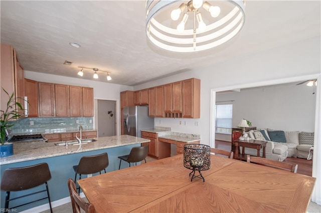 kitchen with ceiling fan, a peninsula, a kitchen bar, stainless steel refrigerator with ice dispenser, and a sink