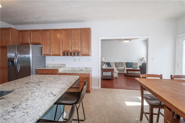 kitchen featuring brown cabinets, light stone counters, stainless steel refrigerator with ice dispenser, and a kitchen breakfast bar