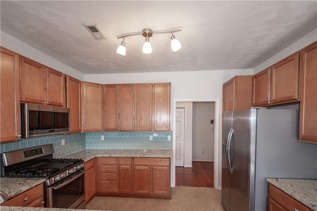 kitchen with visible vents, brown cabinetry, decorative backsplash, light stone counters, and stainless steel appliances