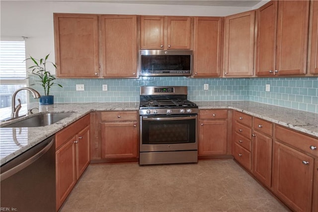 kitchen featuring stainless steel appliances, backsplash, brown cabinetry, a sink, and light stone countertops