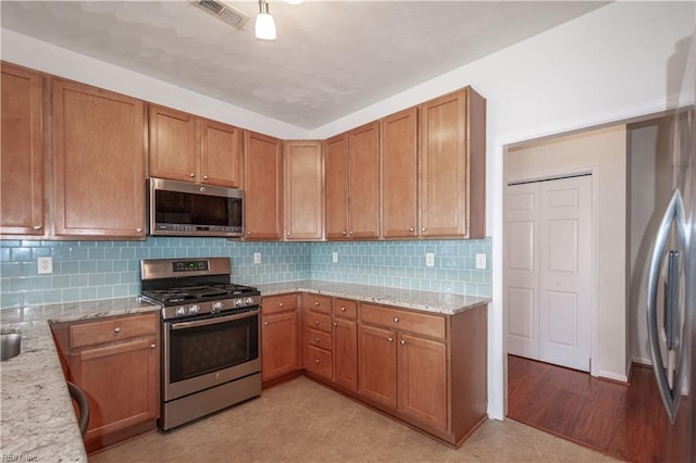 kitchen featuring visible vents, brown cabinetry, appliances with stainless steel finishes, light stone countertops, and backsplash