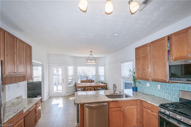 kitchen with brown cabinets, stainless steel appliances, tasteful backsplash, a sink, and a peninsula