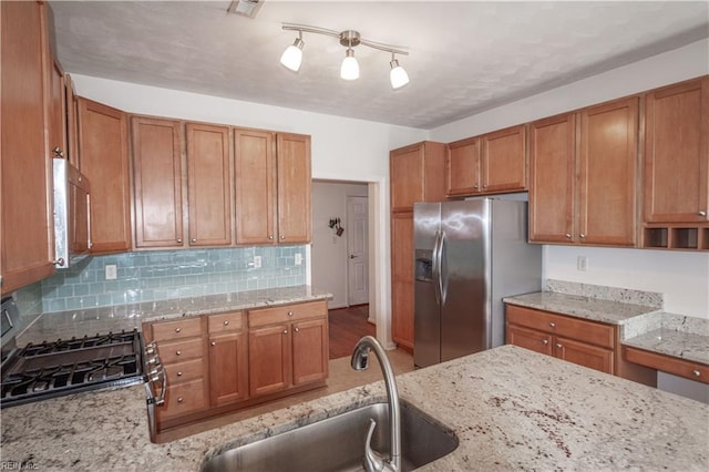 kitchen featuring light stone counters, stainless steel appliances, a sink, tasteful backsplash, and brown cabinetry