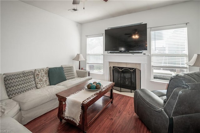 living area featuring ceiling fan, a tiled fireplace, wood finished floors, and visible vents