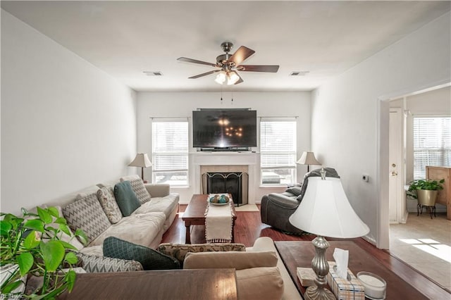 living room featuring wood finished floors, a fireplace with flush hearth, visible vents, and a ceiling fan