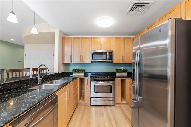 kitchen with visible vents, dark stone counters, appliances with stainless steel finishes, light wood-style floors, and a sink