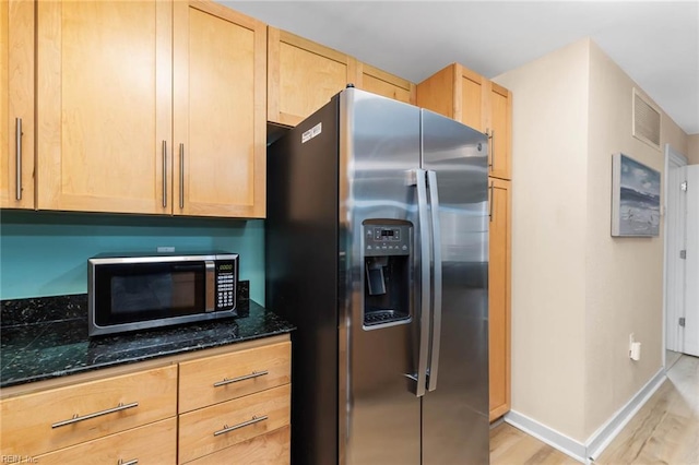 kitchen featuring stainless steel appliances, visible vents, light brown cabinetry, light wood finished floors, and dark stone countertops