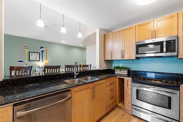 kitchen with light brown cabinets, a sink, light wood-style floors, appliances with stainless steel finishes, and dark stone countertops