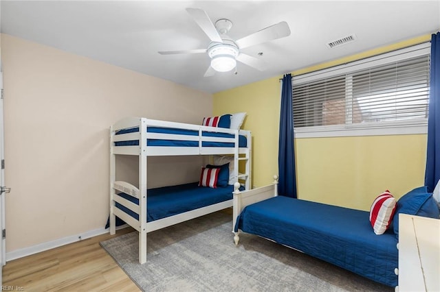 bedroom with a ceiling fan, wood finished floors, visible vents, and baseboards