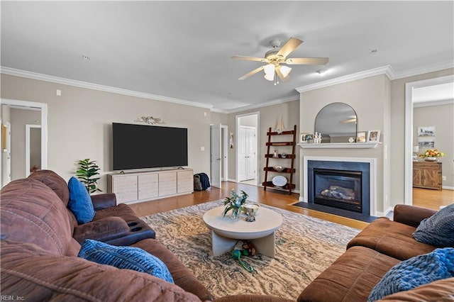 living room featuring a fireplace with flush hearth, ornamental molding, wood finished floors, and a ceiling fan