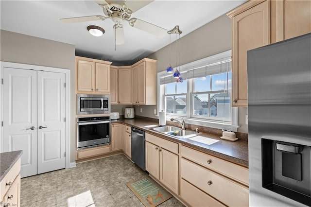 kitchen with stainless steel appliances, dark countertops, a sink, and light brown cabinetry