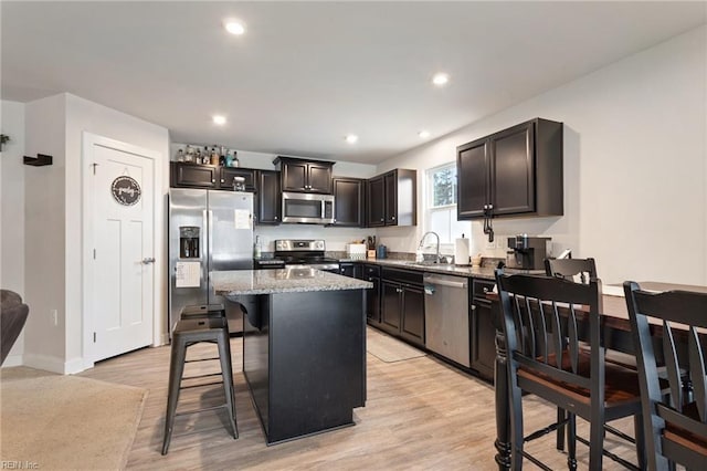 kitchen with light wood-type flooring, light stone counters, a center island, stainless steel appliances, and a breakfast bar area