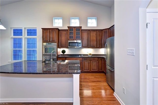 kitchen featuring a center island with sink, light wood-style flooring, appliances with stainless steel finishes, a sink, and dark stone countertops