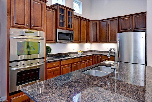 kitchen featuring dark stone countertops, glass insert cabinets, stainless steel appliances, and a sink