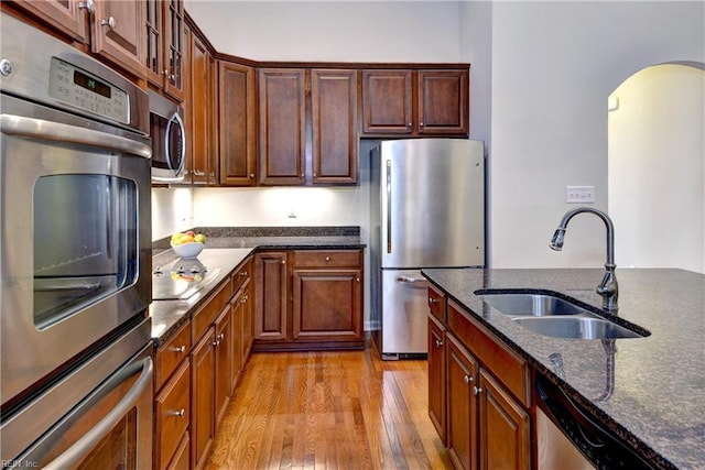 kitchen featuring stainless steel appliances, light wood-style flooring, glass insert cabinets, a sink, and dark stone countertops