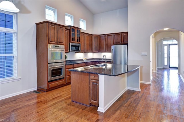 kitchen featuring arched walkways, a towering ceiling, appliances with stainless steel finishes, a sink, and wood finished floors