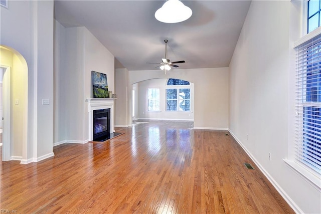 unfurnished living room with arched walkways, visible vents, light wood-style floors, a glass covered fireplace, and ceiling fan