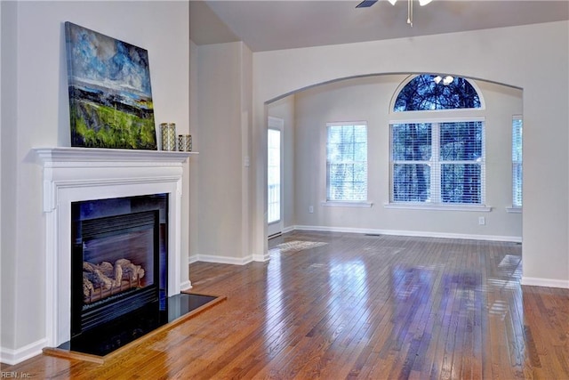 unfurnished living room featuring a glass covered fireplace, baseboards, ceiling fan, and hardwood / wood-style floors