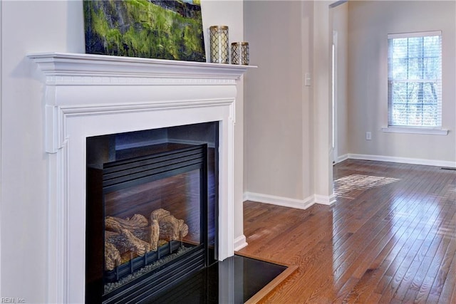 interior details featuring a glass covered fireplace, baseboards, and wood finished floors