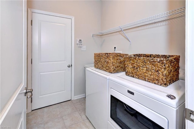 clothes washing area with laundry area, light tile patterned floors, baseboards, and washing machine and clothes dryer