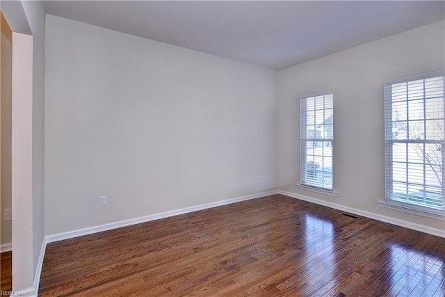 spare room with baseboards, visible vents, and wood finished floors