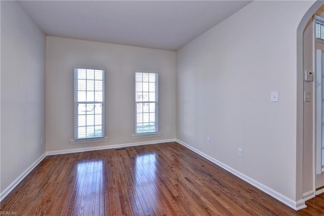 spare room featuring arched walkways, dark wood-type flooring, and baseboards