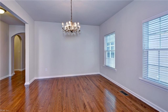 empty room with baseboards, visible vents, arched walkways, dark wood-style floors, and an inviting chandelier