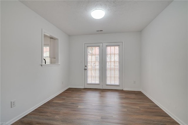 empty room featuring plenty of natural light, a textured ceiling, visible vents, and wood finished floors