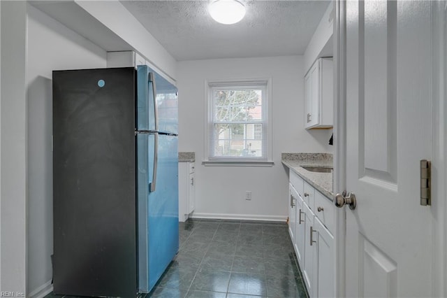 kitchen with a textured ceiling, baseboards, white cabinets, freestanding refrigerator, and light stone countertops