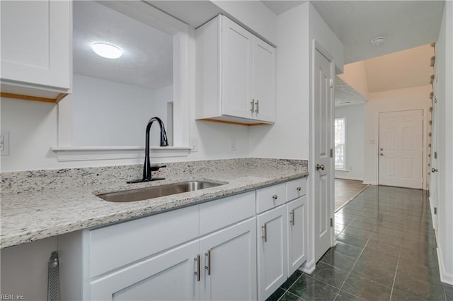 kitchen with light stone counters, dark tile patterned floors, a sink, baseboards, and white cabinets