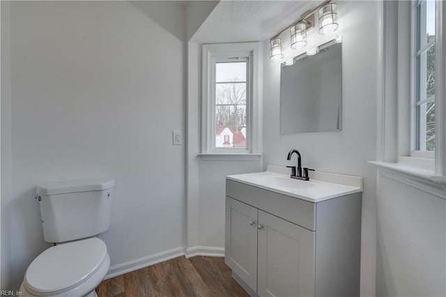 half bathroom featuring vanity, wood finished floors, toilet, and baseboards