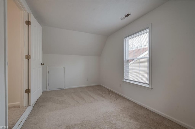 additional living space featuring lofted ceiling, baseboards, visible vents, and light colored carpet