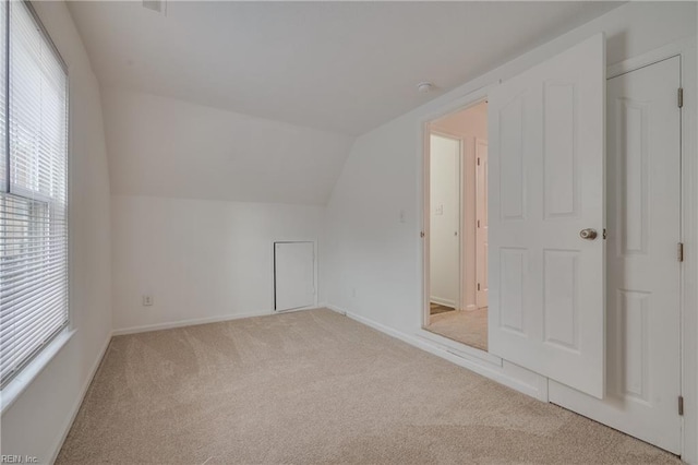 additional living space featuring light carpet, vaulted ceiling, and baseboards