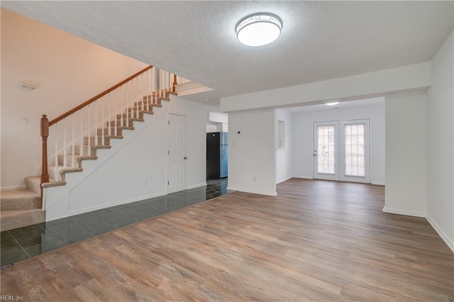 unfurnished living room featuring stairs, a textured ceiling, wood finished floors, and baseboards