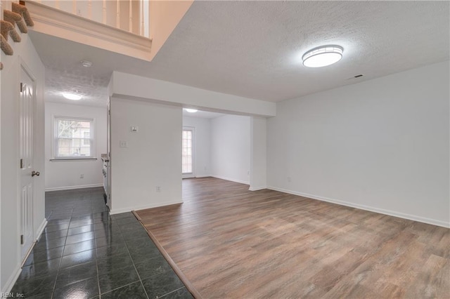 empty room with a textured ceiling, dark wood-style floors, and baseboards