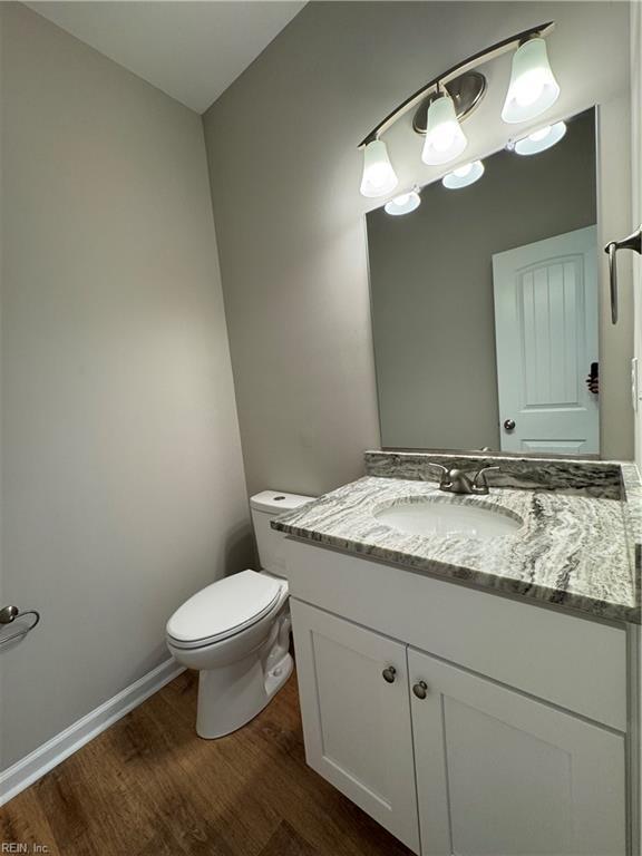 half bathroom featuring baseboards, vanity, toilet, and wood finished floors