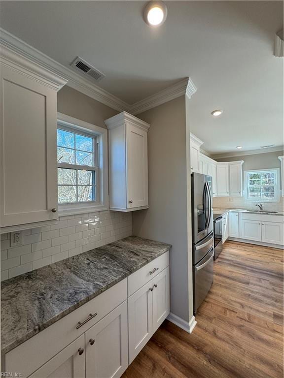 kitchen with dark wood finished floors, crown molding, stainless steel refrigerator with ice dispenser, visible vents, and white cabinetry